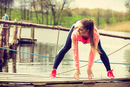 Sports and activities concept. Slim fit attractive woman exercising stretching outdoor. Young motivated girl training in sporty clothes on lake shoreの写真素材