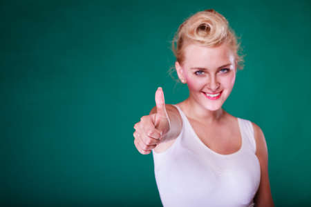 Symbols, gestures concept. Smiling young woman with pinup hair making thumb up gesture. Studio shot on green backgroundの写真素材