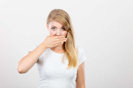 Saying bad things, shocking news concept. Ashamed young blonde woman having hand on her mouth....