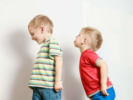 Free time, fun and independence. Little boys play together indoors brother stick tongue out. Blonde children wear colorful clothes.の写真素材
