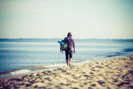 Man hiker backpacker walking with backpack on sea shore at sunny day. Adventure, summer, tourism active lifestyle. Young long haired guy trampingの写真素材