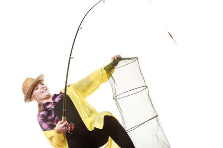 Spinning, angling, cheerful fisherwoman concept. Happy woman in yellow raincoat holding fishing rod and keepnet having fun.の写真素材