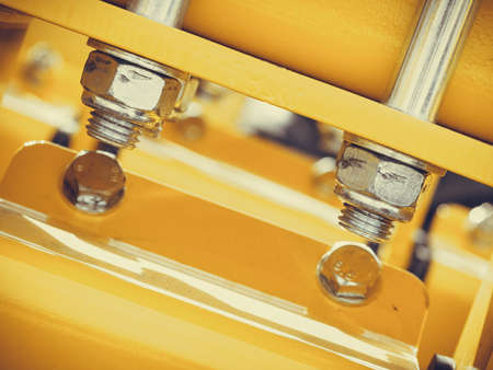 Construction machines concept. Detailed closeup of screws and bolts on yellow indrustrial machineryの写真素材