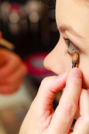 Visage concept. Close up woman getting make up on eyelids. Applying eyeshadow with brush, opened...