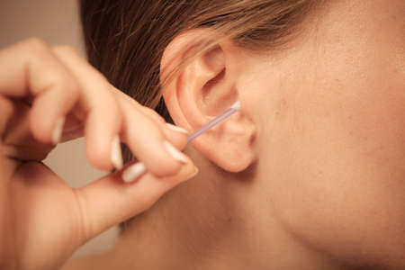 Hygiene concept. Woman cleaning ear with cotton swabs closeupの写真素材