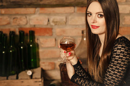 Elegant beauty lady long hair full make up wearing black dress tasting wine in rural cottage interior cellerの写真素材