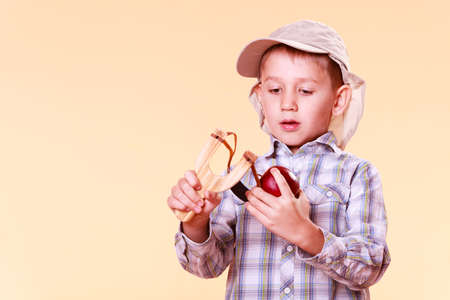 Nature and free time prankster little boy. Child have fun with  wooden sling shot and fruit hold apple.の写真素材