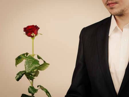 Smart clothing for guys. Elegant young man with red rose. Handsome boy wearing black classic suit and white shirt.の写真素材