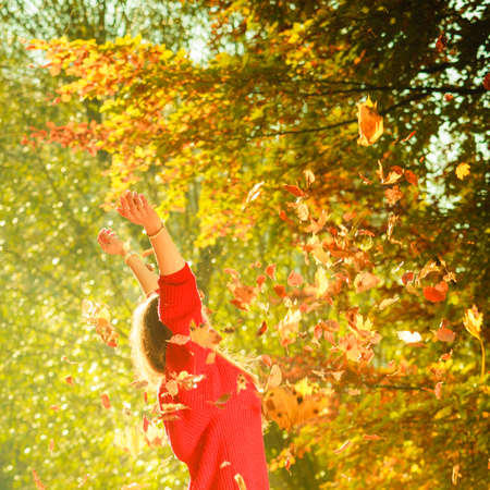 Autumn time. Fun and carefree. Cheerful lovely young woman playing with leaves. Girl relax in autumnal park forest surrounded by trees with flying leaf.の写真素材