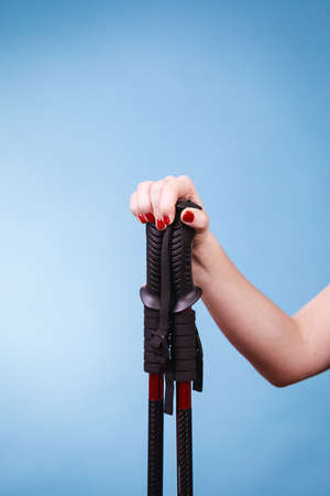 Woman hand holding ski poles or nordic walking sticks. Winter sport activity on blue studio shot の写真素材