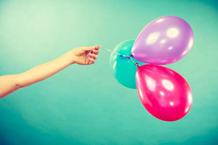 Female hand holding colorful balloons. Summer holidays, celebration and lifestyle concept. Studio shot green backgroundの写真素材