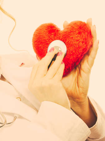 Medical examination of cardiology. Cardiologist with heart and stethoscope. Female doctor in white uniform makes measurement heartbeat. Filtered.の写真素材