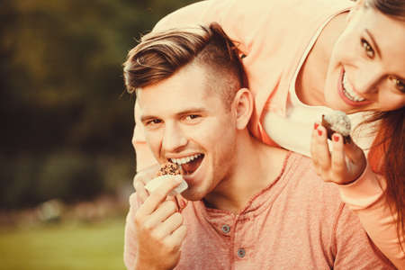 Love and happiness. Young lovely couple eating cupcakes cookies. Smiling people with sweet food spending time in park garden.の写真素材