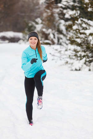 Girl wearing sportswear and running on snow with trees in background, front view. Winter sports, outdoor fitness, workout, health concept.の写真素材
