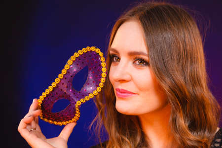 People celebration concept. Masquerade. Beautiful girl holding carnival mysterious mask on darkの写真素材