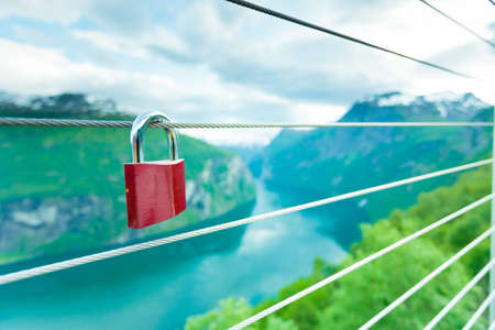 Tourism vacation and travel. Red love lock padlock on bridge and mountains, view over magical Geirangerfjorden from Flydalsjuvet viewpoint, Norway Scandinavia.の写真素材
