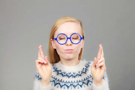 Gestures and signs concept. Teenage blonde woman making promise gesture with fingers crossed.の写真素材