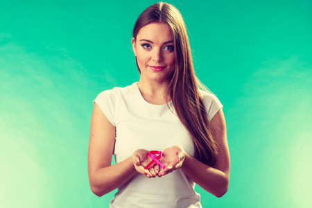 Healthcare and medicine concept - woman showing pink breast cancer awareness ribbon on hands, against green tealの写真素材