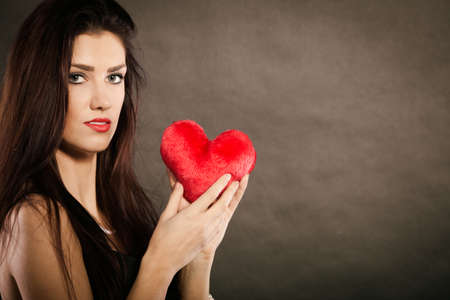 Woman brunette long hair girl wearing black sensual dress holding gift in form of red heart love...