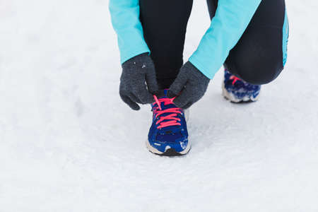 Winter sports fashion concept. Tying sport fitness shoes in snow, footwear for workout outside