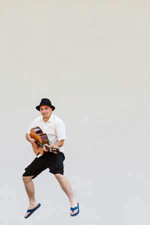Music passion, hobby concept. Man in sun hat jumping and playing on guitarの写真素材