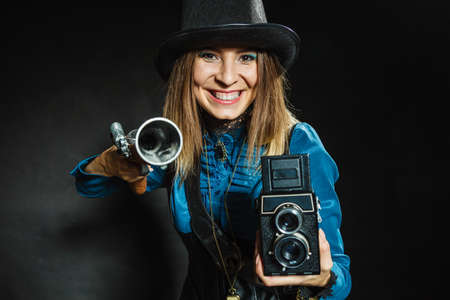 Photography and retro style. Young vintage attractive girl holds old aged camera. Steampunk photographer with gun pistol.の写真素材