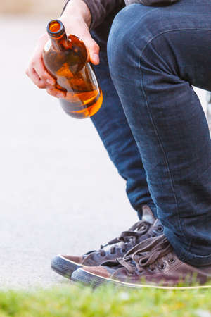 Man depressed with wine bottle sitting on bench outdoor. People abuse and alcoholism problems.の写真素材