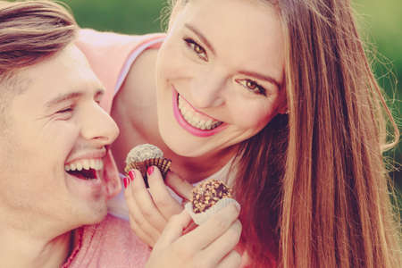 Love and happiness. Cute lovely lovers feeding each other by cupcakes cookies. Smiling couple with sweet food having fun.の写真素材