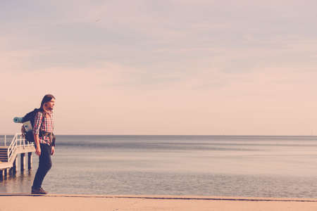 Man hiker backpacker walking with backpack by seaside at sunny day. Adventure, summer, tourism active lifestyle. Young long haired guy trampingの写真素材