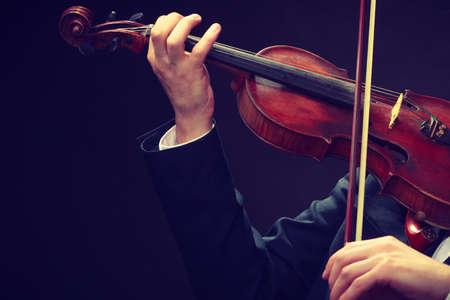 Music passion, hobby concept. Close up young man man dressed elegantly playing on wooden violin. Studio shot on dark backgroundの写真素材
