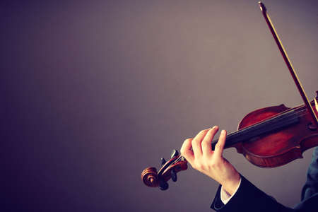 Music passion, hobby concept. Close up young man man dressed elegantly playing on wooden violin. Studio shot on dark backgroundの写真素材