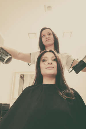 Hairdresser drying dark female hair using professional hairdryer, heat modelingの写真素材