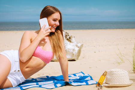 Technology and communication. Happy smiling woman with mobile phone calling to people friends. Young attractive girl talking by smartphone on beach.の写真素材
