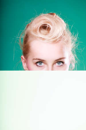Woman standing behind white board at eye level, half face only. Studio shot on blue green backgroundの写真素材