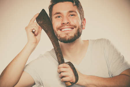 Young man with shaving having fun with machete large knife. Handsome guy removing face beard hair. Skin care and hygiene humor.の写真素材