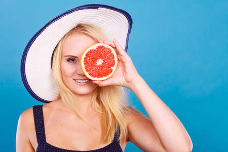 Healthy diet, refreshing food full of vitamins. Woman wearing sun hat holding sweet delicious red grapefruit fruitの写真素材