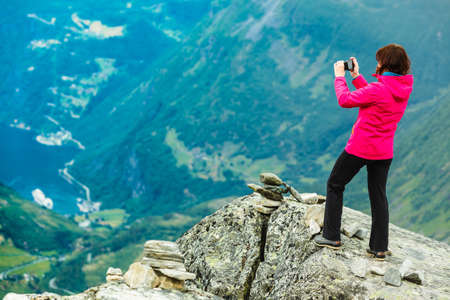 Tourism vacation and travel. Female tourist taking photo with camera, enjoying Geiranger fjord and mountains landscape from Dalsnibba Plateau viewpoint, Norway Scandinavia.の写真素材