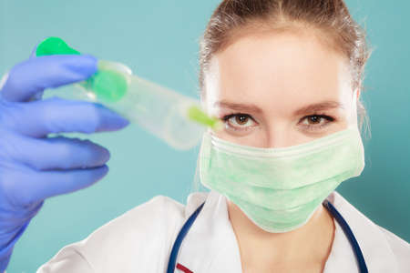 Medication and cure. Injection concept. Young woman doctor holding syringe. Female specialist with mask on face and vaccine in hand.の写真素材
