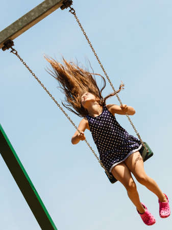 Craziness and freedom. Young summer girl playing on swing-set outdoor. Crazy playful child swinging very high to touch the sky.の写真素材