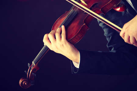 Music passion, hobby concept. Close up young man man dressed elegantly playing on wooden violin. Studio shot on dark backgroundの写真素材