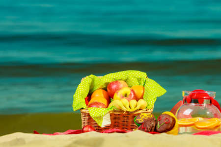Relaxation during summertime concept. Picnic basket with fruit on red blanket near sea,の写真素材