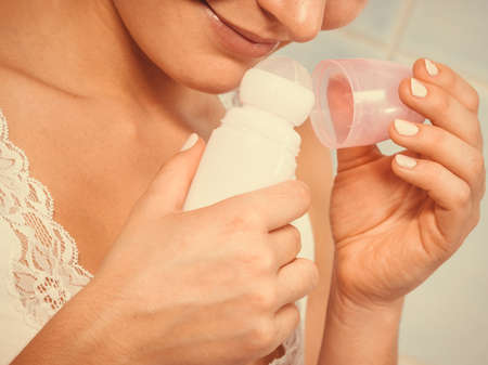 Woman holding stick deodorant in hands. Girl in bathroom with antiperspirant cosmetics. Daily skin care and hygiene.の写真素材