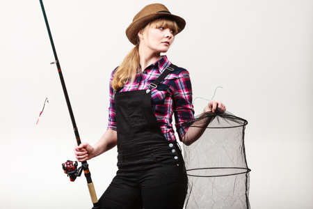 Spinning, angling, cheerful fisherwoman concept. Happy woman in sun hat holding fishing rod and keepnet having fun.の写真素材