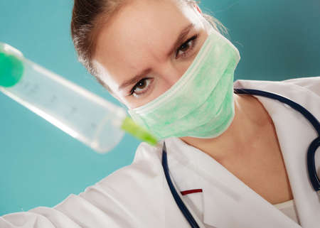 Medication and cure. Injection concept. Young woman doctor holding syringe. Female specialist with mask on face and vaccine in hand.の写真素材