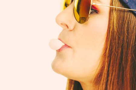 Fun leisure people concept. Funky girl blowing balloon. Chewing bubblegum. Young lady has beautiful sunglasses.の写真素材