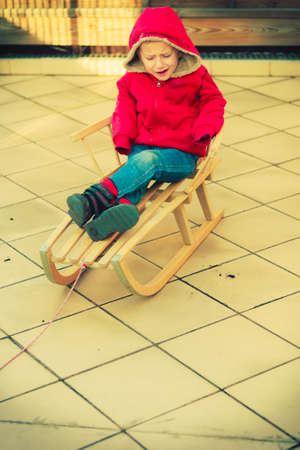 childhood kids imagination concept dissatisfied little young boy playing outside on sled but there...