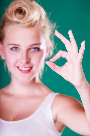 Symbols, gestures concept. Smiling young woman with pin up hair making a ok gesture. Studio shot on green backgroundの写真素材