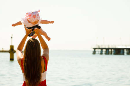 Summer family recreation concept. Mother holding and playing with little baby on beach during summertime.の写真素材