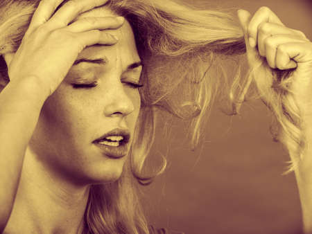 Haircare, health problem concept. Unhappy sad woman looking at damaged split ends on her blonde hair. Sepiaの写真素材