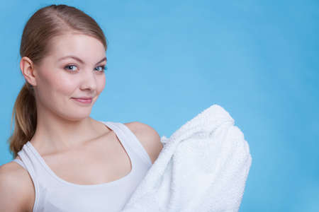 Workout, hygiene concept. Smiling woman holding a big white clean towel, studio shot on blue backgroundの写真素材